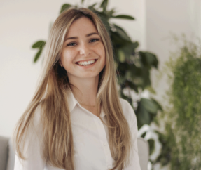 Portrait von Katrin Kramer. Eine junge Frau mit professionellem Outfit lächelt in die Kamera. 